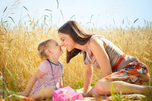 Photo: Happy young mother with little daughter on field in summer day Happy young mother with little daughter on field in summer day