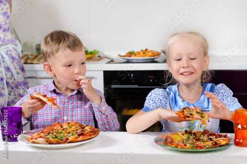 Photo: Happy little boy and girl eating Italian pizza Happy little boy and girl eating Italian pizza