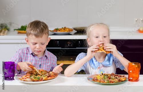 Photo: Happy little boy and girl eating Italian pizza Happy little boy and girl eating Italian pizza