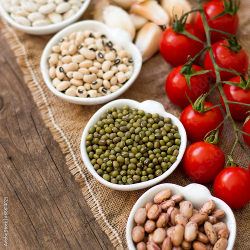 Photo: Legumes in bowls, tomatoes, garlic and olive oil on wooden table Legumes in bowls, tomatoes, garlic and olive oil on wooden table