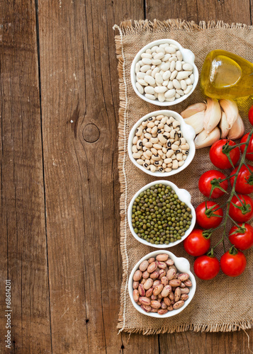 Photo: Legumes in bowls, tomatoes, garlic and olive oil on wooden table Legumes in bowls, tomatoes, garlic and olive oil on wooden table