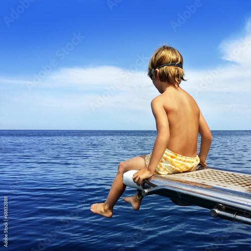 Instant Collection: Boy sitting on boat bridge looking at the sea Boy sitting on boat bridge looking at the sea