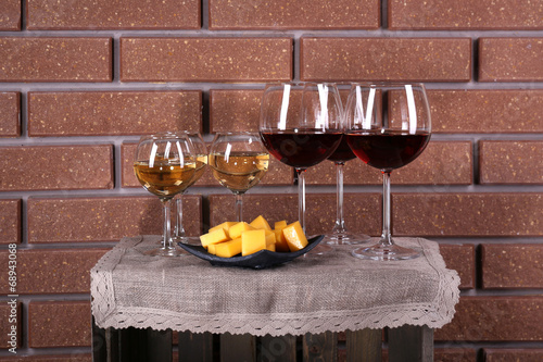 Photo: Glasses of wine and cheese on box on brick wall background Glasses of wine and cheese on box on brick wall background
