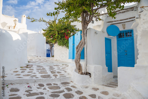 Fototapeta Mykonos traditional white streetview with blue door and trees, Greece