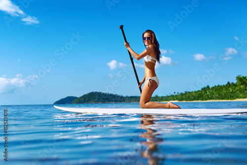 Plakat Rekreacyjne sporty wodne. Zdrowy szczęśliwy sprawny kobieta z seksownym ciałem wiosłowaniu, klęcząc na Stand Up Paddle, Surf Board In Sea. Wakacje letnie Wakacje podróżnicze. Aktywny styl życia. Spędzania wolnego czasu. Hobby
