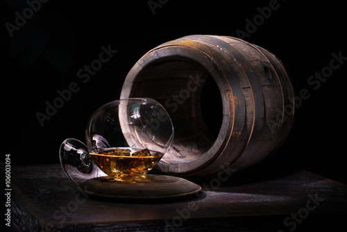 Glass with alcohol and ice on a background of empty oak barrels