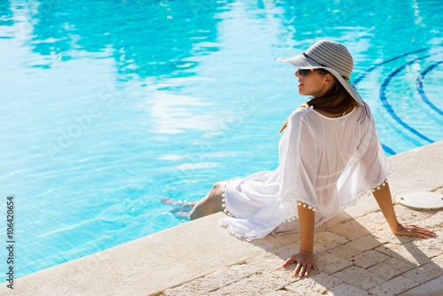 Plakat Fasonuje pięknej kobiety relaksuje przy luksusowym kurortu zdroju poolside na wakacje. Młoda modna dama jest ubranym słońce kapelusz i białego kaftan.