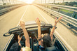 Happy couple driving on the road into the sunset in a sports car Happy couple driving on the road into the sunset in a sports car