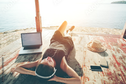 Zdjęcie XXL Młoda kobieta z laptop odpoczynkową i słuchającą muzyką z hełmofonami blisko oceanu. Zamierzone światło słoneczne i kolor vintage