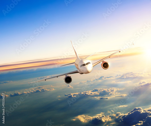 Fototapeta Airplane flying above clouds in dramatic sunset