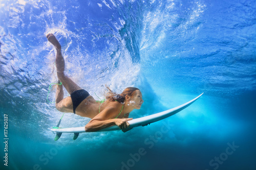 Plakat Młoda aktywna dziewczyna w bikini w akci - surfingowiec z kipieli deską nurkuje podwodnego pod łamać dużą ocean fala. Rodzinny styl życia, ludzie obóz sportów wodnych przygoda, plaża ekstremalne pływać na letnie wakacje