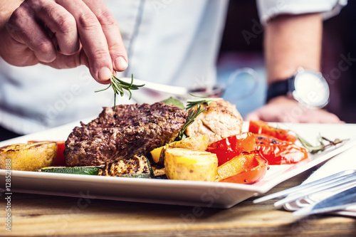 Fotoobraz na płótnie Szef kuchni w hotelowej lub restauracyjnej kuchni gotuje tylko ręki. Przygotowany stek wołowy z dekoracją roślinną.