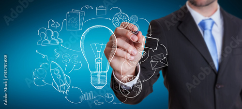 Businessman drawing a lightbulb with a pen with multimedia icons