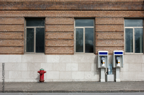 Lonely street with one red and green fire hydrant and two public pay telephones.
