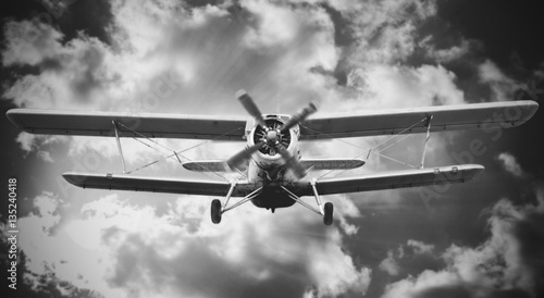 Fototapeta Biplane landing with cloudy sky on the background. Black and whi