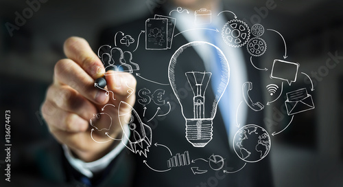 Businessman drawing a lightbulb with a pen with multimedia icons