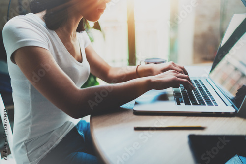 Young attractive woman working at home on modern computer.Girl typing on notebook keyboard while sitting at the wooden table at home.Blurred background, flares.
