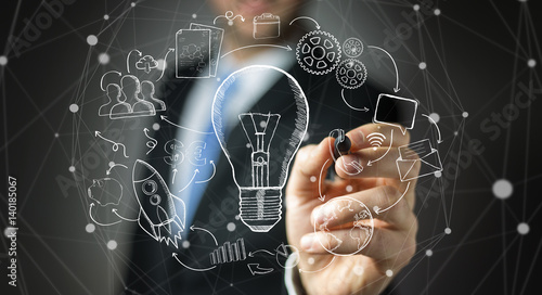 Businessman drawing a lightbulb with a pen with multimedia icons