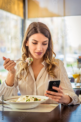 Plakat Młodej kobiety łasowania sałatka przy restauracją i texting na smartphone