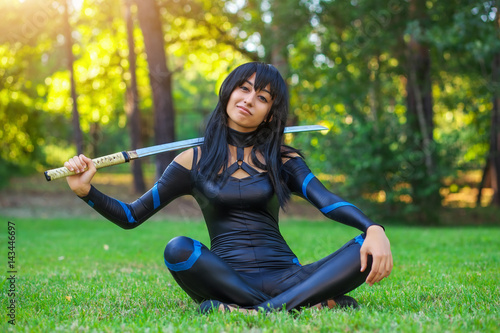 Plakat Młoda dziewczyna siedzi na trawie i trzyma miecz samurajski. Oryginalny charakter cosplay