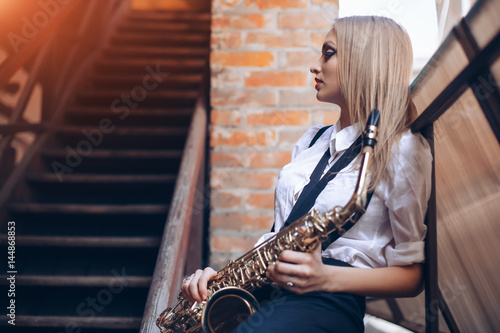Fotoobraz na płótnie Profilowa portret młoda atrakcyjna dziewczyna w białej koszula z saksofonem - plenerowym w starym miasteczku. Sexy młoda kobieta z sax myślenia o czymś