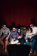 Group of young friends in 3d glasses have fun entertainment watching tv show on couch together, top view. Red curtain background with free space. Group of young friends in 3d glasses have fun entertainment watching tv show on couch together, top view. Red curtain background with free space.