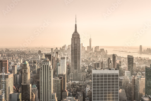 Fototapeta New York City. Manhattan downtown skyline with sun illuminated Empire State Building and skyscrapers at sunset.