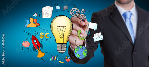 Businessman drawing a lightbulb with a pen with multimedia icons