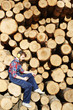 Side view portrait of lumberjack using smartphone on break from work on timber cutting site sitting on tree trunks Side view portrait of lumberjack using smartphone on break from work on timber cutting site sitting on tree trunks