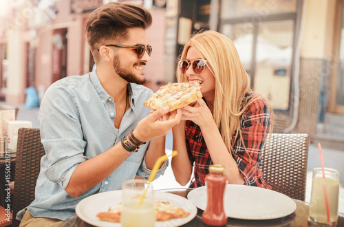 Plakat Piękna młoda para siedzi w kawiarni i jedzenie pizzy. Konsumpcjonizm, jedzenie, koncepcja stylu życia