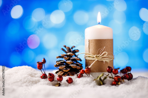 Candle and christmas decoration in snow with blue light background.