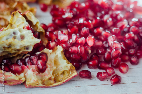 Pomegranate peel and seeds over white wooden background.