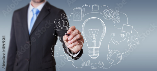 Businessman drawing a lightbulb with a pen with multimedia icons