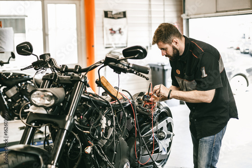 Zdjęcie XXL Profesjonalny mechanik motocykl pracuje w serwisie naprawy rowerów. Mechanik sprawdzanie poziomu baterii rower woltomierz w garażu
