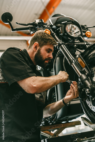 Zdjęcie XXL Profesjonalny mechanik odkręca przednie koło motocykla. Rower jest na wyciągu na stacji obsługi.