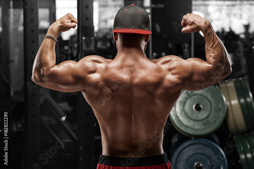 Plakat Tylni widoku mięśniowy mężczyzna pozuje w gym, seans plecy i bicepsach. Silny męski nagi tors, wypracowany