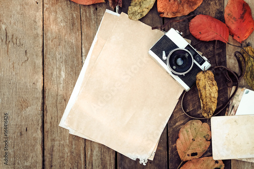 Retro camera and empty old instant paper photo album on wood table with maple leaves in autumn border design - concept of remembrance and nostalgia in fall season. vintage rustic style. © jakkapan
