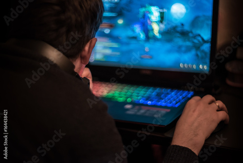 Plakat Mężczyzna siedzi przy laptopie i gra w gry wideo w ciemnym pokoju. Młody gamer gra wideo noszenie słuchawek.