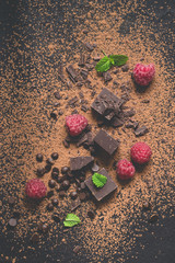 Pieces of dark chocolate, powder, drops and raspberries. Food dessert background.