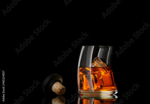 close up view of glass of  whiskey and cork on black back