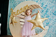 Beautiful little girl in a dress posing next to wooden moon decoration with golden star pillows. Beautiful little girl in a dress posing next to wooden moon decoration with golden star pillows.