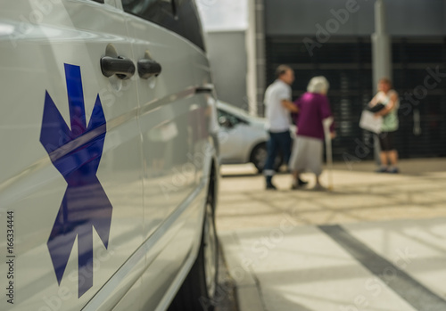 Plakat Pogotowie z gwiazdą życia przed szpitalem i seniorem z kulą - Krankenwagen z Gwiazdą życia dla Krankenhaus und Seniorin mit Gehhilfe