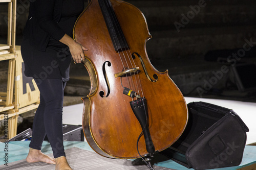 Plakat Szczegóły kontrabasu, instrument muzyczny rodziny strunowych łuków. Basista układa instrument muzyczny i ma go oddać przed rozpoczęciem koncertu.