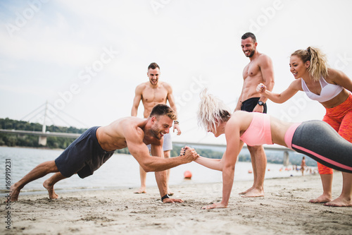 Plakat Grupują młodych atrakcyjnych ludzi ma zabawę na plaży i robi niektóre sprawności fizycznej trening.