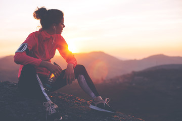 Athletic woman resting after a hard training in the mountains at sunset. Sport tight clothes.