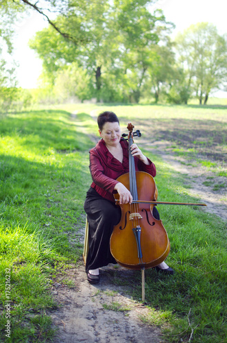 Plakat Dorosła muzyk kobieta bawić się na violoncello outdoors. Nauczyciel muzyki gra na wiolonczeli