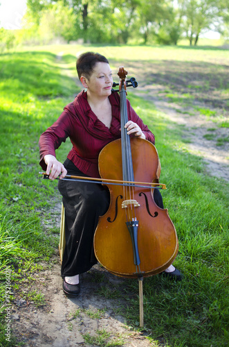 Plakat Dorosła muzyk kobieta bawić się na violoncello outdoors. Nauczyciel muzyki gra na wiolonczeli