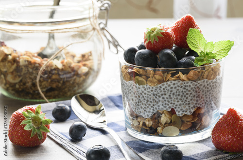 Plakat Jogurt z granola, świeże jagody, nasiona chia i owies w szklance na tle drewna. ścieśniać