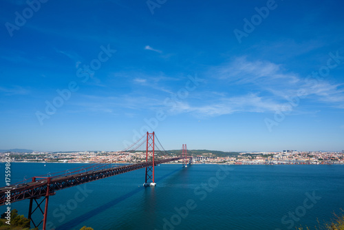 Plakat Czerwony most 25 de abril most w Lisbon Portugalia nad Tagus rzeką przy jasnym pogodnym letnim dniem