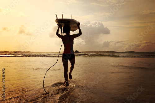 Plakat Tylni widok młoda kobieta surfingowiec z białym surfboard odprowadzeniem morze